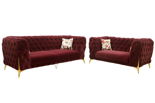A pair of luxurious, tufted burgundy velvet sofas with elegant gold legs. Each sofa is adorned with floral-patterned cushions, creating a rich and inviting atmosphere.