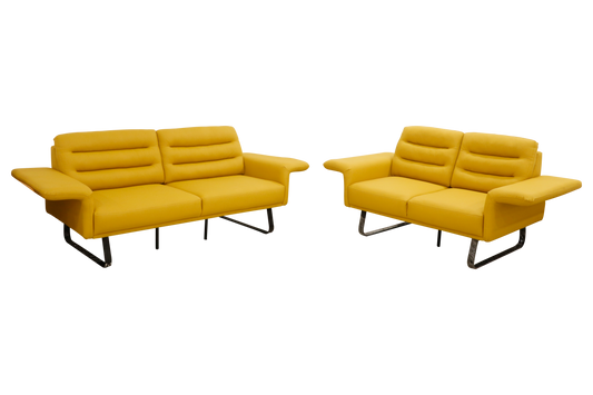 A modern yellow sofa with padded backrests and wide armrests, featuring black metal legs, set against a plain blue background.